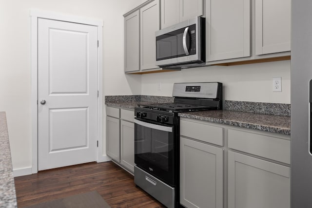 kitchen with dark stone counters, stainless steel appliances, dark wood-type flooring, and gray cabinetry