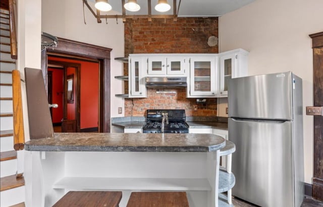 kitchen featuring white cabinets, black range, stainless steel fridge, kitchen peninsula, and a breakfast bar area