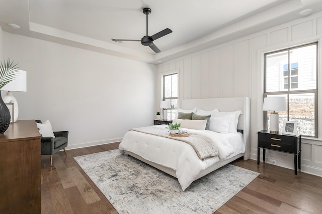 bedroom featuring ceiling fan, dark hardwood / wood-style flooring, and a tray ceiling