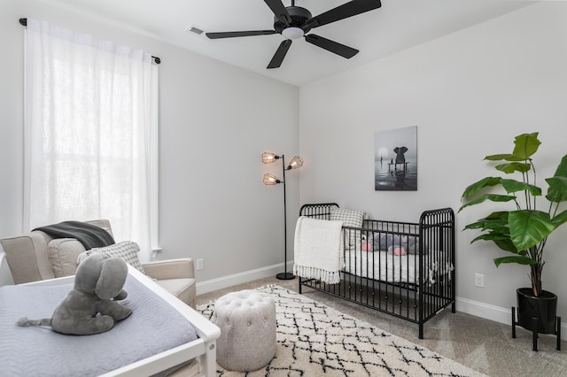 carpeted bedroom featuring a crib and ceiling fan