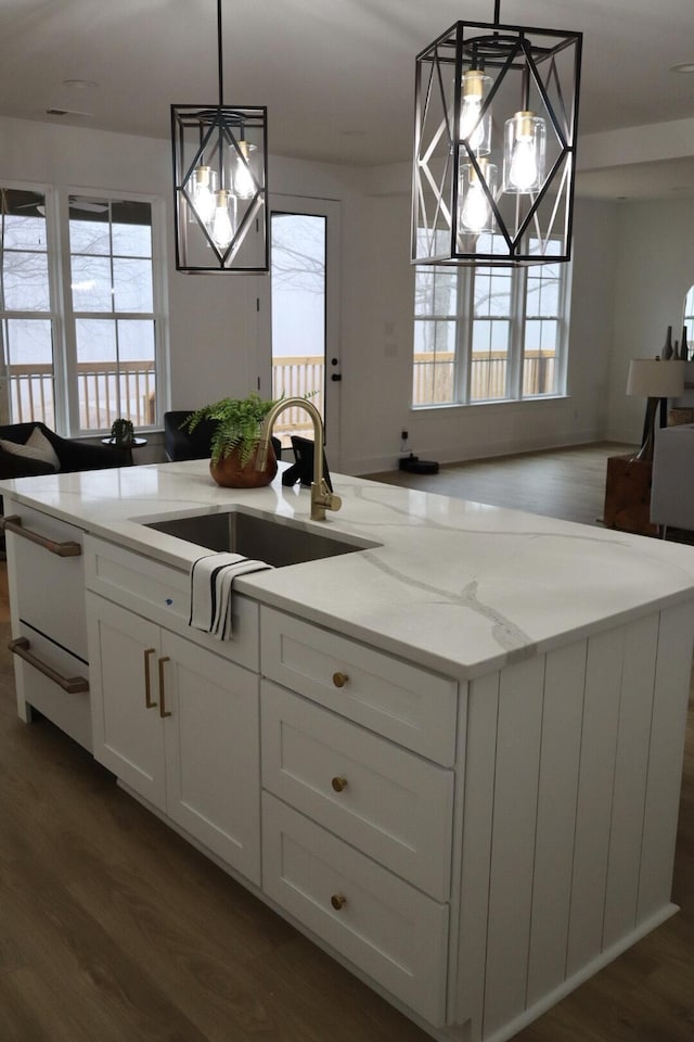 kitchen with pendant lighting, dark hardwood / wood-style flooring, light stone counters, white cabinets, and sink