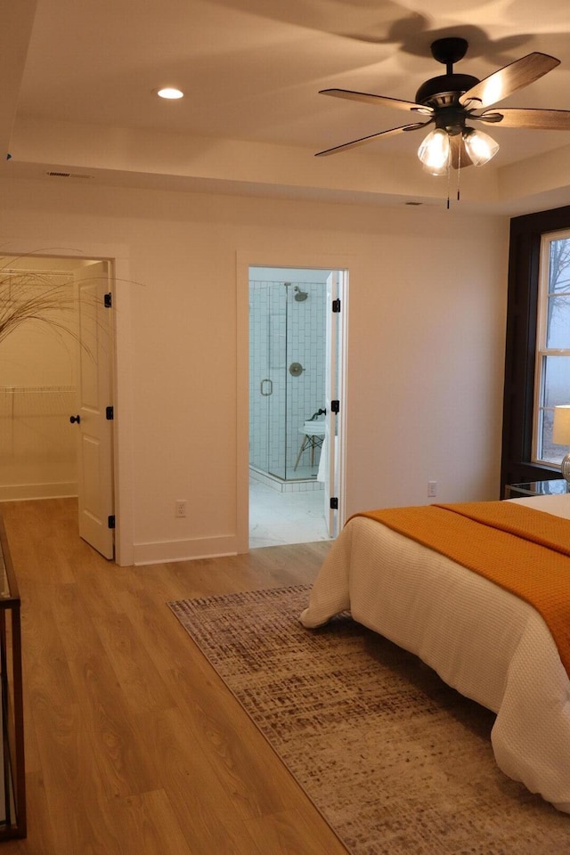 bedroom with light hardwood / wood-style floors, ceiling fan, and a tray ceiling