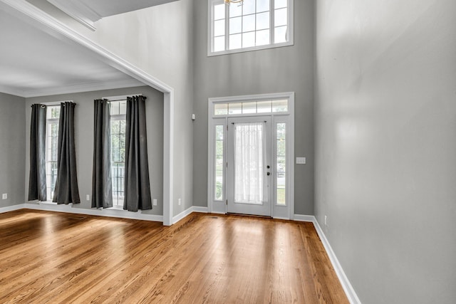 foyer entrance with a healthy amount of sunlight, light hardwood / wood-style floors, crown molding, and a towering ceiling