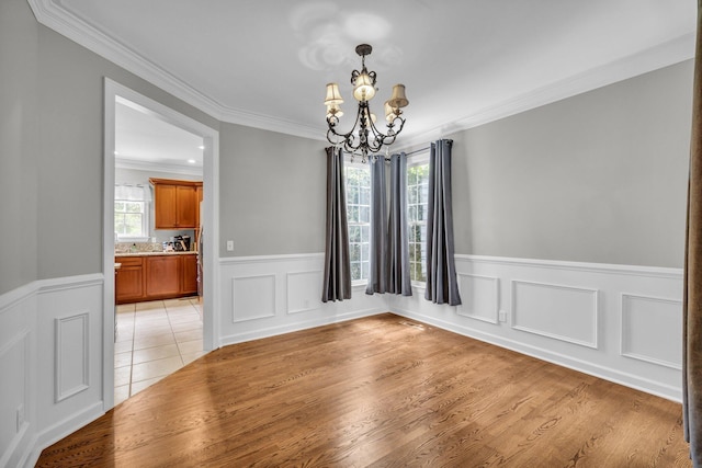 unfurnished dining area featuring ornamental molding, light hardwood / wood-style flooring, a healthy amount of sunlight, and an inviting chandelier