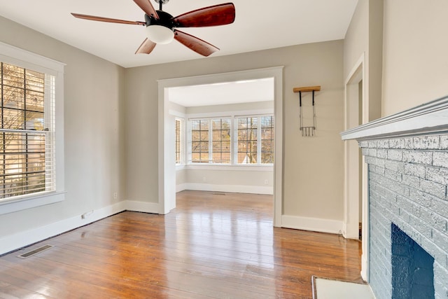 unfurnished living room with wood finished floors, a fireplace, baseboards, and a healthy amount of sunlight