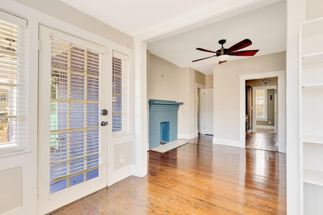 interior space with light wood-style flooring, a fireplace, baseboards, and ceiling fan