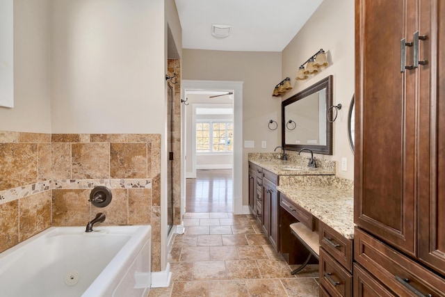 bathroom with a tub with jets, a stall shower, vanity, and baseboards