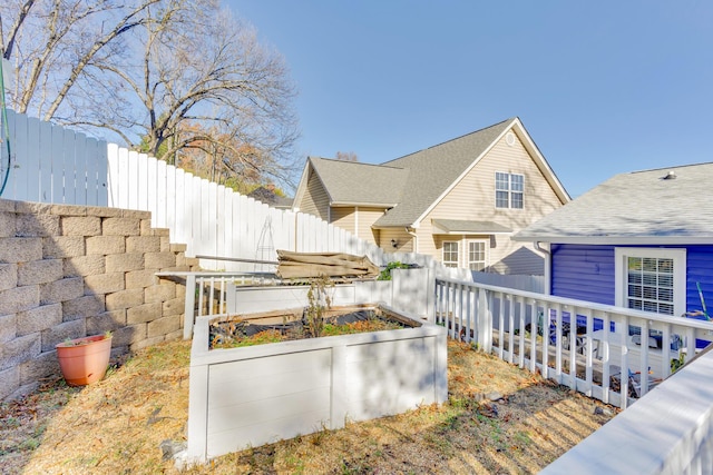 view of side of home with a vegetable garden, fence, and roof with shingles