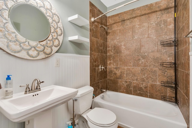 bathroom featuring a sink, toilet, shower / washtub combination, and wainscoting