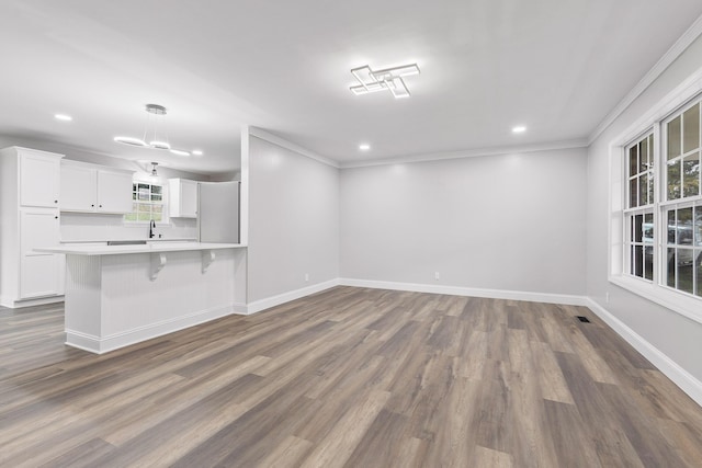 interior space featuring a kitchen breakfast bar, kitchen peninsula, crown molding, dark hardwood / wood-style flooring, and white cabinetry