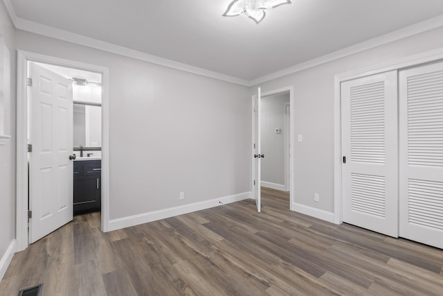 unfurnished bedroom featuring dark wood-type flooring, sink, ornamental molding, connected bathroom, and a closet