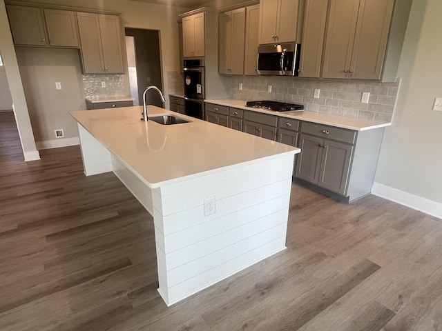 kitchen with a kitchen island with sink, sink, decorative backsplash, wood-type flooring, and stainless steel appliances