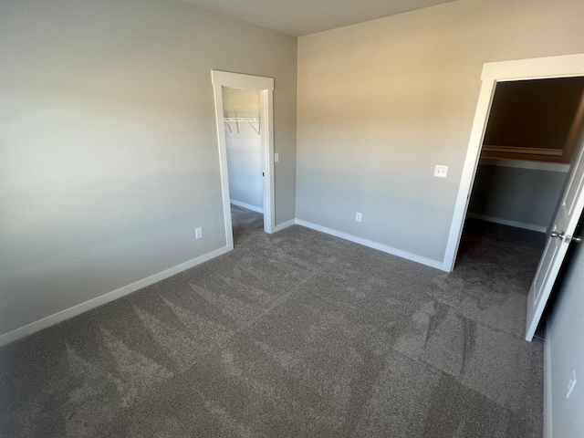 unfurnished bedroom with a spacious closet, a closet, and dark colored carpet