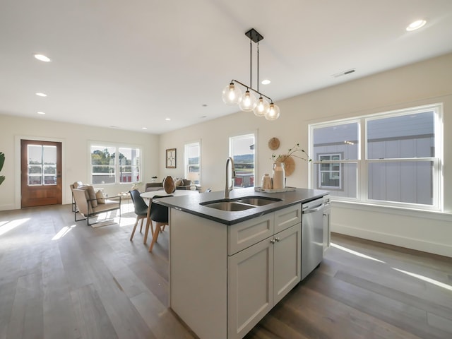 kitchen featuring dark wood-type flooring, sink, dishwasher, hanging light fixtures, and an island with sink