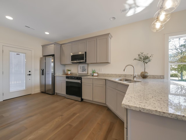 kitchen with stainless steel appliances, light hardwood / wood-style flooring, kitchen peninsula, decorative light fixtures, and gray cabinets