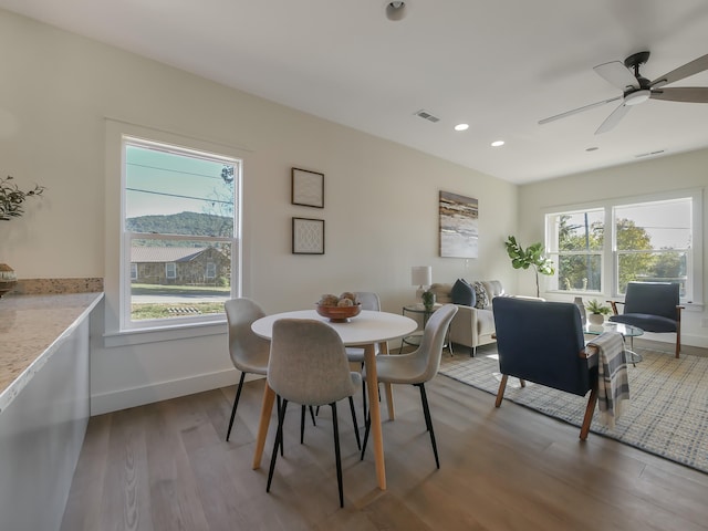 dining area with ceiling fan, light hardwood / wood-style floors, a mountain view, and a wealth of natural light