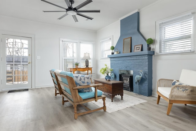 sitting room featuring ceiling fan, light hardwood / wood-style floors, a wood stove, and ornamental molding