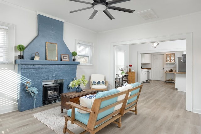 living area featuring ceiling fan, a wood stove, crown molding, and light hardwood / wood-style flooring