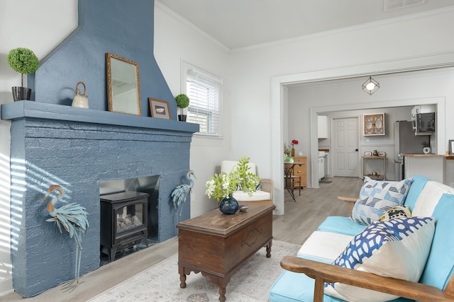 living room featuring light hardwood / wood-style flooring, a wood stove, and crown molding