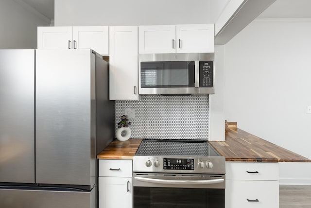 kitchen with white cabinets, butcher block counters, stainless steel appliances, and ornamental molding