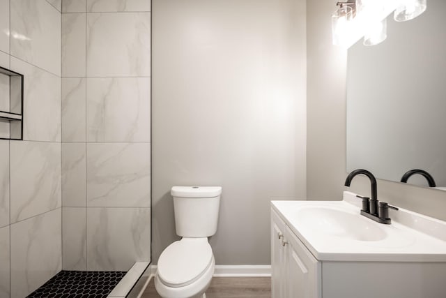 bathroom featuring vanity, wood-type flooring, tiled shower, and toilet