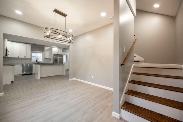 kitchen with white cabinetry, decorative backsplash, hanging light fixtures, stainless steel appliances, and light hardwood / wood-style flooring