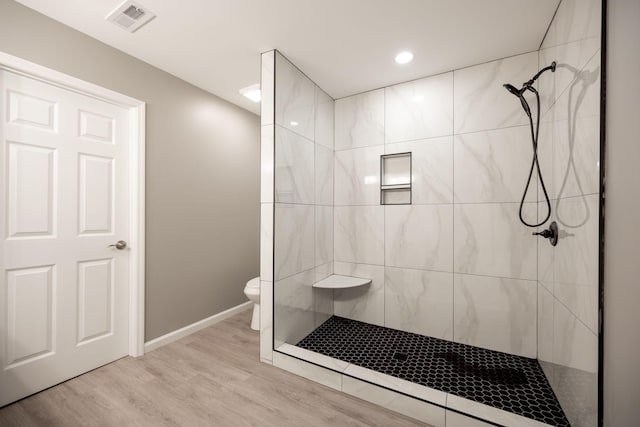 bathroom with wood-type flooring, tiled shower, and toilet