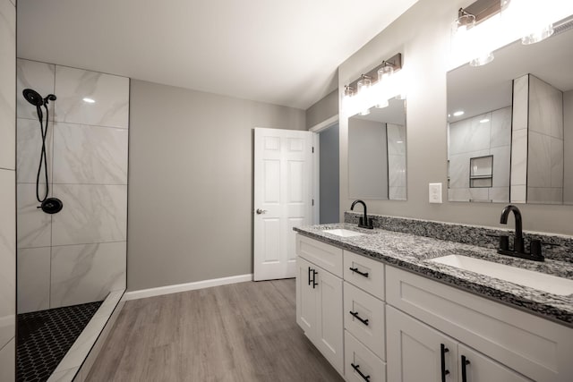 bathroom with wood-type flooring, tiled shower, and vanity