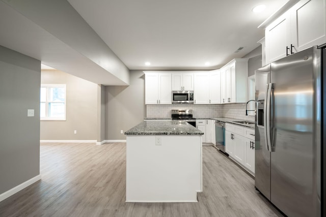 kitchen featuring sink, dark stone counters, a kitchen island, stainless steel appliances, and white cabinets