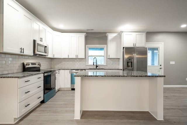 kitchen featuring white cabinetry, appliances with stainless steel finishes, a center island, and dark stone counters