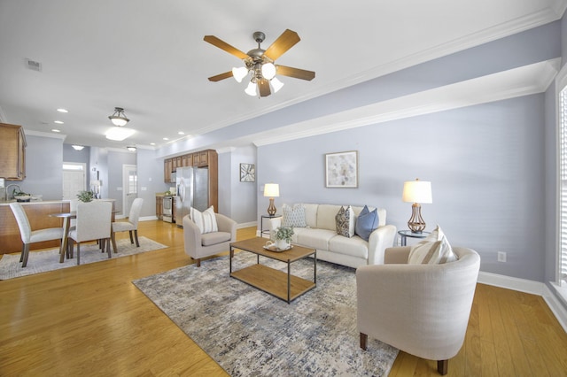 living room with ceiling fan, a healthy amount of sunlight, ornamental molding, and light hardwood / wood-style flooring