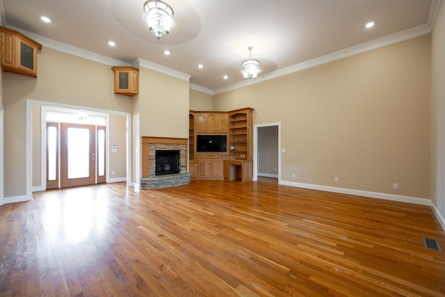 unfurnished living room with a stone fireplace, ornamental molding, a towering ceiling, light hardwood / wood-style floors, and a chandelier