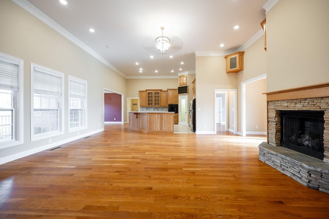 unfurnished living room featuring a notable chandelier, light hardwood / wood-style floors, a stone fireplace, and ornamental molding