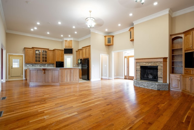 unfurnished living room featuring a notable chandelier, light hardwood / wood-style floors, a stone fireplace, and crown molding