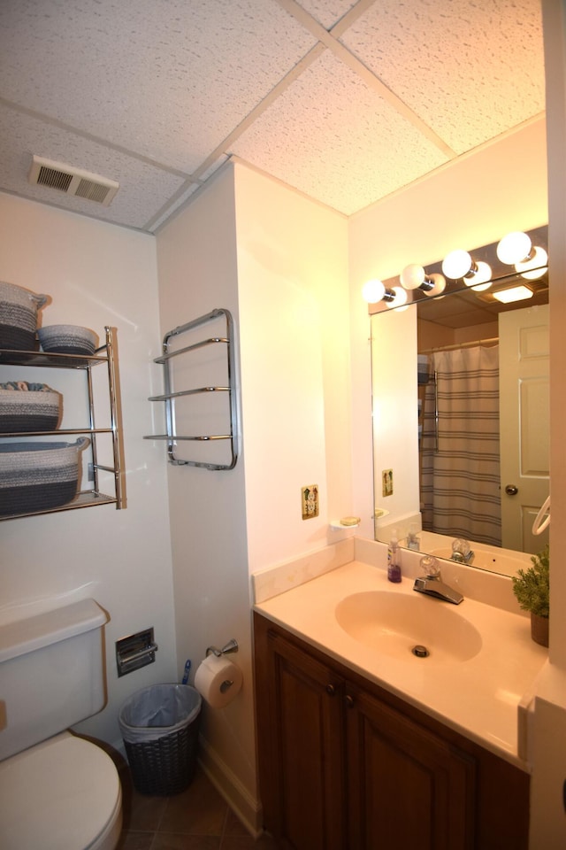 bathroom featuring a paneled ceiling, tile patterned flooring, vanity, and toilet