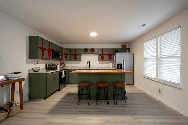 kitchen featuring wood counters, a kitchen breakfast bar, stainless steel appliances, sink, and light hardwood / wood-style flooring