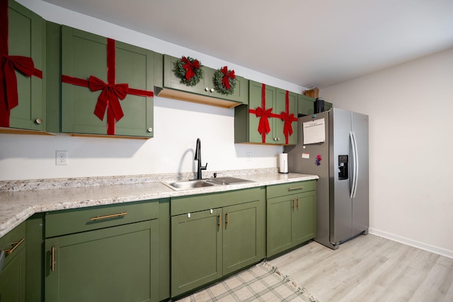 kitchen with stainless steel fridge, light wood-type flooring, green cabinetry, and sink