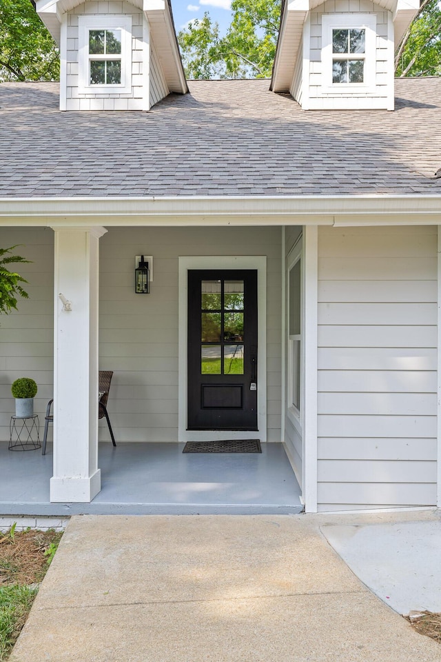 view of exterior entry with a porch and roof with shingles