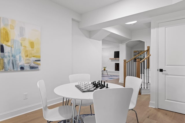 dining area with light wood finished floors, a fireplace, stairs, and baseboards