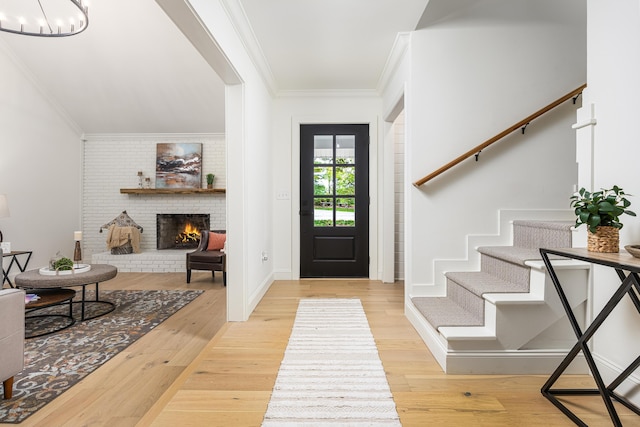 entrance foyer featuring wood finished floors, crown molding, a brick fireplace, a chandelier, and stairs