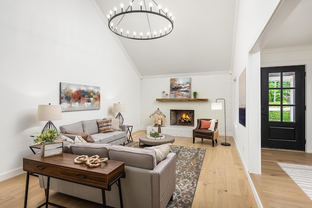 living area with high vaulted ceiling, ornamental molding, an inviting chandelier, light wood finished floors, and a brick fireplace