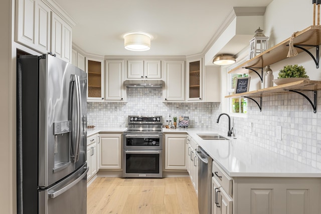 kitchen with under cabinet range hood, light wood-type flooring, light countertops, stainless steel appliances, and a sink