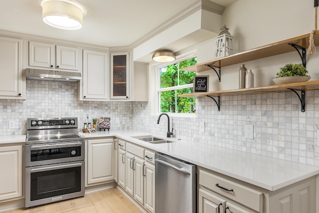 kitchen featuring tasteful backsplash, under cabinet range hood, light countertops, appliances with stainless steel finishes, and a sink