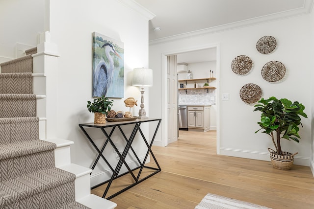 hall featuring baseboards, light wood-style floors, ornamental molding, and stairs