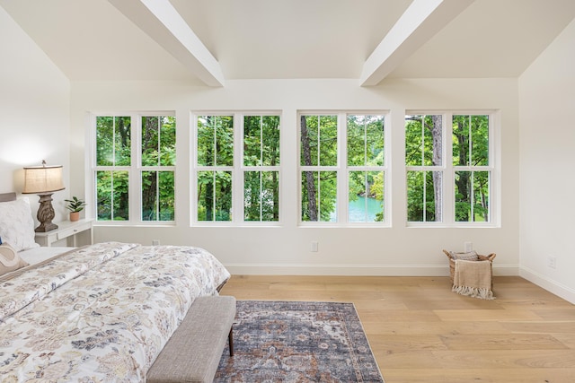 bedroom with multiple windows, baseboards, light wood-type flooring, and vaulted ceiling with beams