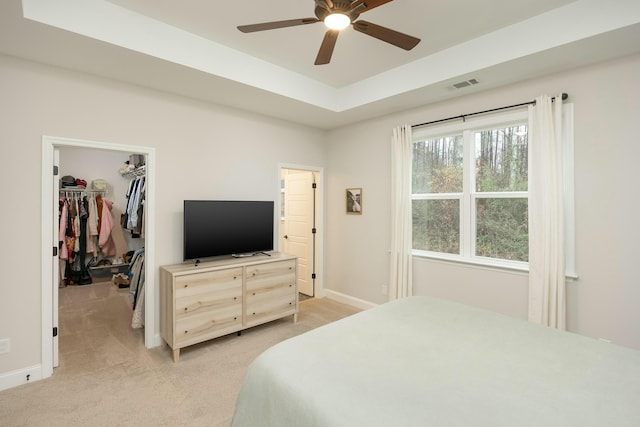 bedroom featuring light colored carpet, a raised ceiling, ceiling fan, a spacious closet, and a closet