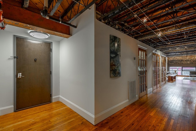 hall with baseboards, visible vents, and hardwood / wood-style floors