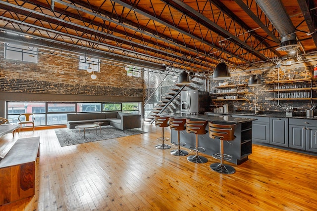 bar with indoor wet bar, light wood-style flooring, stairway, a sink, and high vaulted ceiling