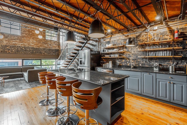 bar with stainless steel appliances, a sink, a towering ceiling, wet bar, and light wood finished floors