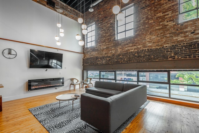 living area with a high ceiling, a glass covered fireplace, hardwood / wood-style floors, and a healthy amount of sunlight